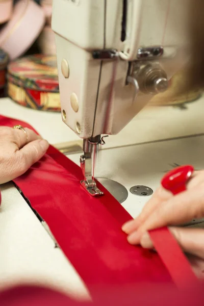 Fita vermelha e pano sendo costurado através de uma máquina de costura — Fotografia de Stock