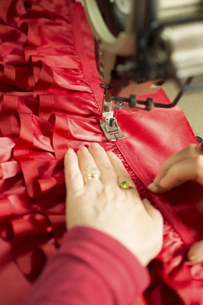 Mãos guiando pano vermelho através da máquina de costura — Fotografia de Stock