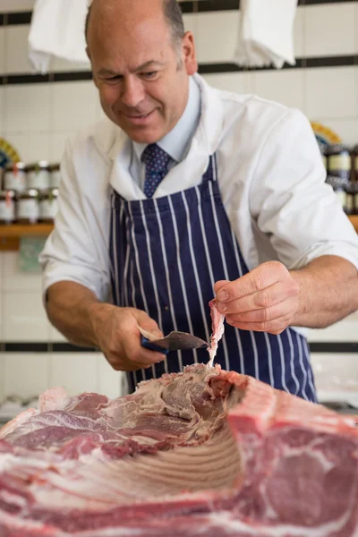 Happy butcher trimming fat off a joint — Stock Photo, Image