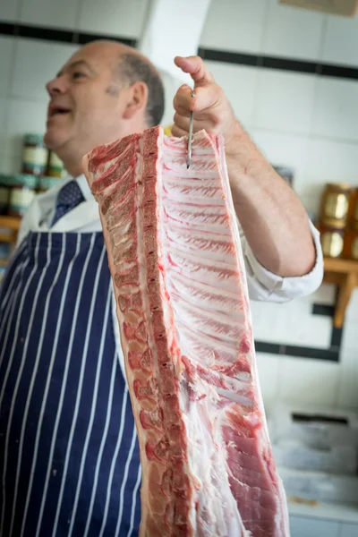 Açougueiro que transporta uma união de carne em um gancho — Fotografia de Stock