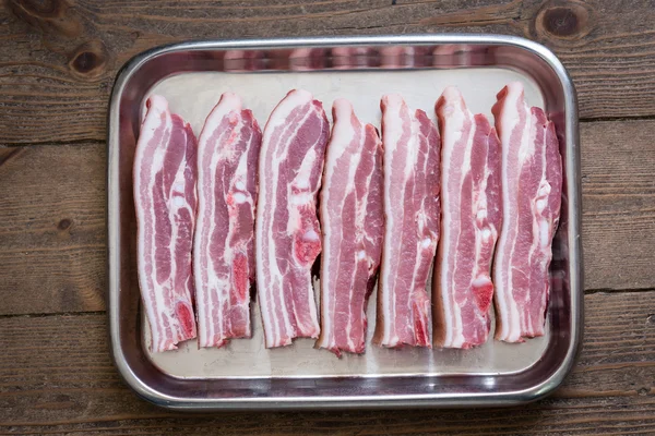 Belly of pork in a silver tray on wooden background — Stock Photo, Image