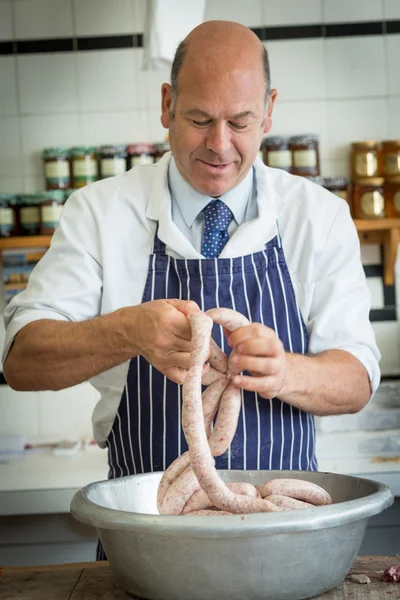 Lächelnder Metzger verknüpft Wurst mit der Hand Stockbild