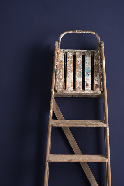 Old Wooden Stepladder Leaning Over a Blue Backdrop