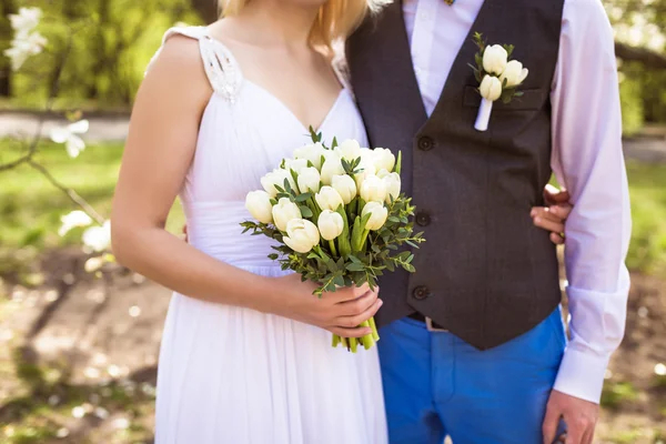 Gelukkige bruid en bruidegom poseren in het park in de buurt van Lentebloemen op trouwdag — Stockfoto