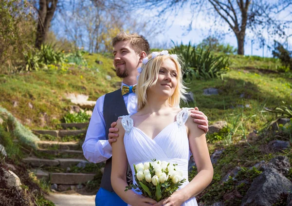 Szczęśliwa panna młoda i pozowanie w parku, w pobliżu wiosenne kwiaty na dzień ślubu pary młodej — Zdjęcie stockowe