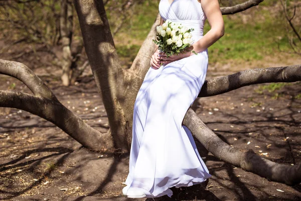 Glückliche Braut posiert am Hochzeitstag im Park in der Nähe von Frühlingsblumen — Stockfoto