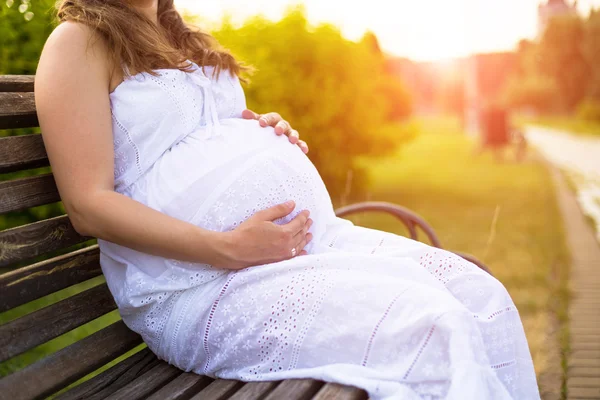 Gravid kvinna sitter på en bänk i soliga sommardag. Koppla av lugn bild Stockfoto