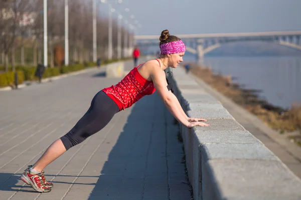 Femme sportive faisant des pompes pendant l'entraînement à l'extérieur du quai de la ville tôt le matin — Photo