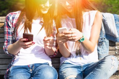 Mutlu genç kızların telefonlarını kullanarak ve having fun yaz parkta genç.