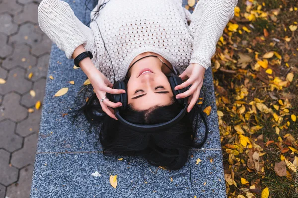 Female student girl outside in park listening to music on headphones — Stock Photo, Image