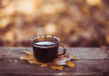 Sıcak kahve ve kırmızı kitap sonbahar yaprakları ile ahşap arka plan - mevsimlik rahatla kavramı