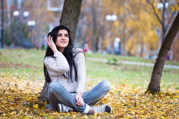 Молодая счастливая девочка-подросток пользуется планшетом и слушает музыку в осеннем городском парке. Осенняя картина в стиле жизни — стоковое фото