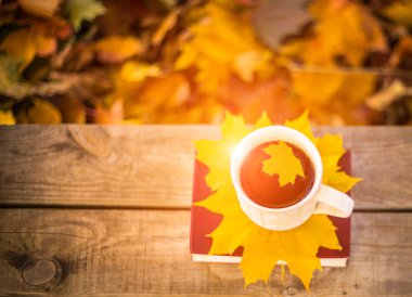 Sıcak kahve ve kırmızı kitap sonbahar yaprakları ile ahşap arka plan üzerinde