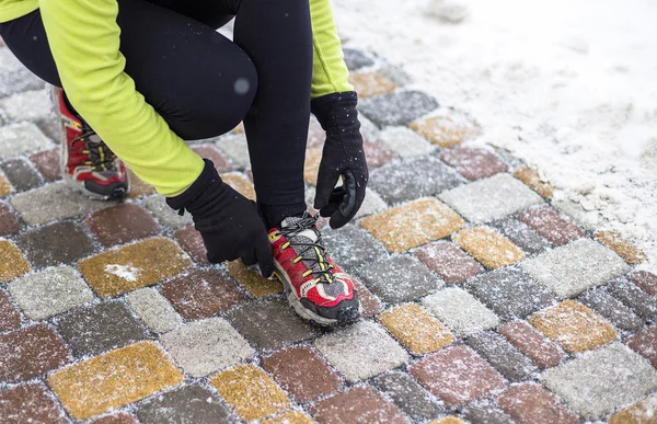 Молодая спортивная модель завязывает кроссовки во время зимних тренировок на улице — стоковое фото