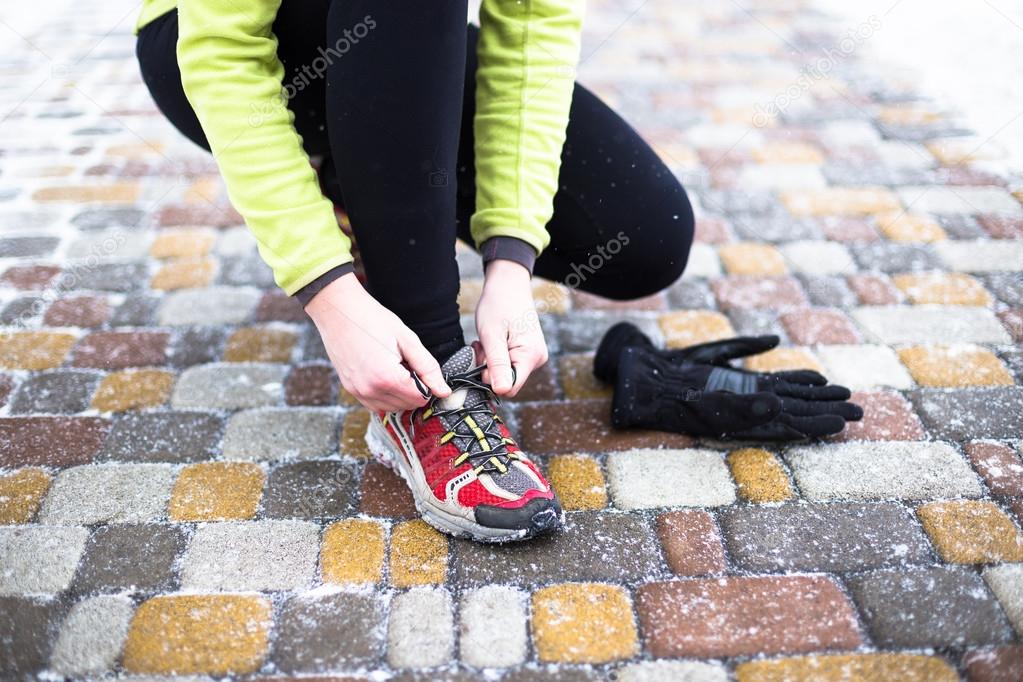 Young sport woman model tying running shoes during winter training outside