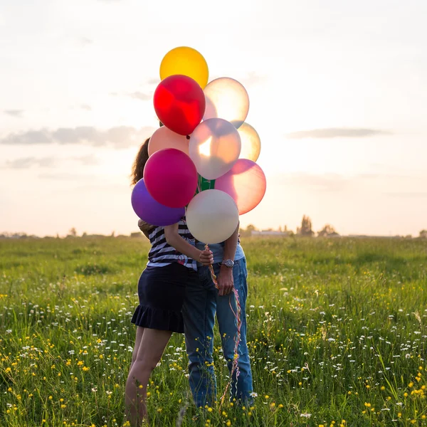 Couple in love are kissing and holding multicolored balloons in beautiful sunset — Stock Photo, Image