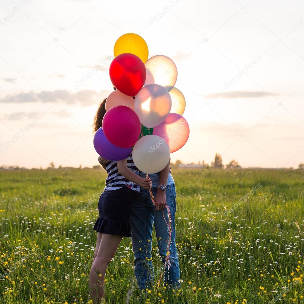 Couple in love are kissing and holding multicolored balloons in beautiful sunset