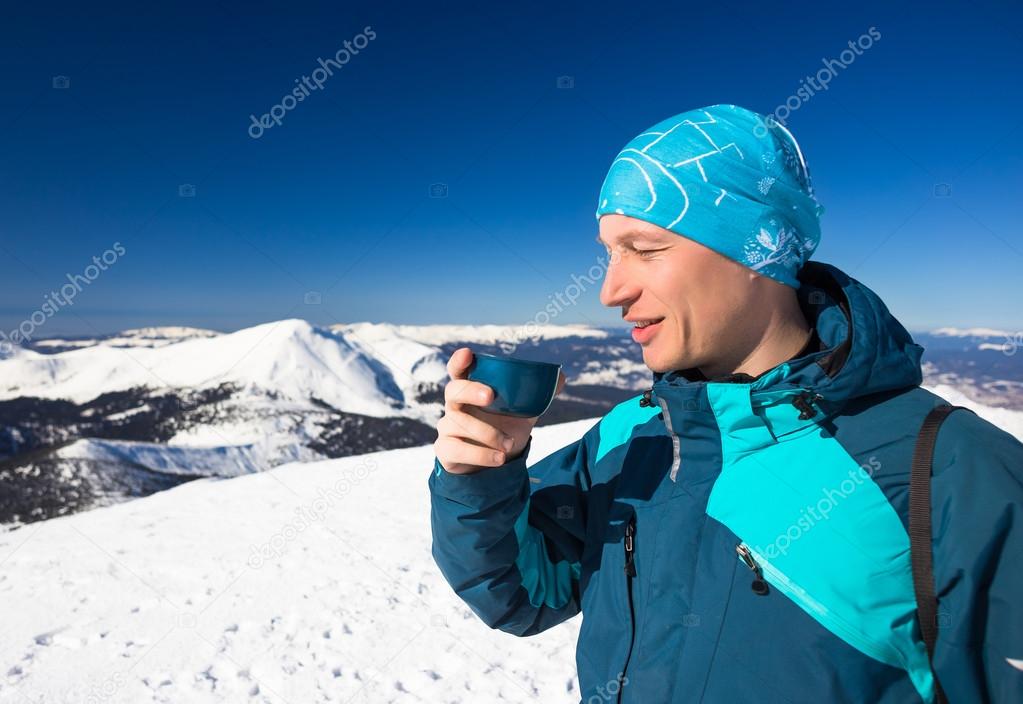 young man drink hot tea during hiking on mountain in winter