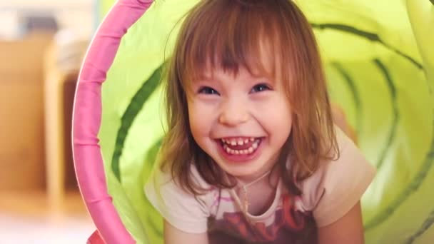 Счастливая маленькая девочка смеется в детском игрушечном тоннеле — стоковое видео