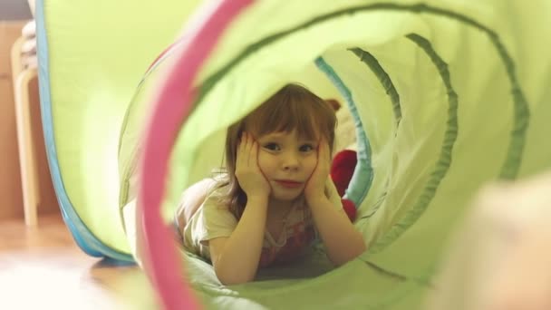 Счастливая маленькая девочка смеется в детском игрушечном тоннеле — стоковое видео