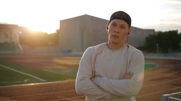 Lentidão do jovem usa fones de ouvido no campo ao pôr do sol na pista do estádio — Vídeo de Stock