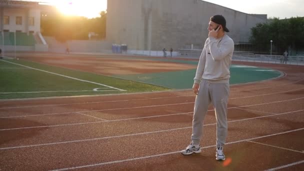Молодой спортсмен говорит по телефону на стадионе трек в замедленной съемке — стоковое видео