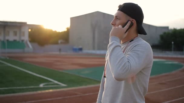 Joven fitness hombre habla por teléfono en pista de estadio en cámara lenta — Vídeos de Stock