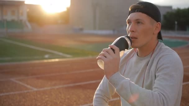 L'athlète fatigué avec une casquette de baseball boit de l'eau de la bouteille sur la piste du stade — Video