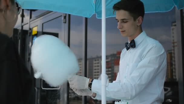 Chico joven haciendo algodón de azúcar en una máquina especial, lleva corbata de lazo, detrás de él globos — Vídeos de Stock