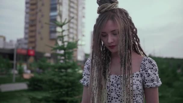 Una linda joven y feliz chica con rastas camina por la calle y posa — Vídeo de stock