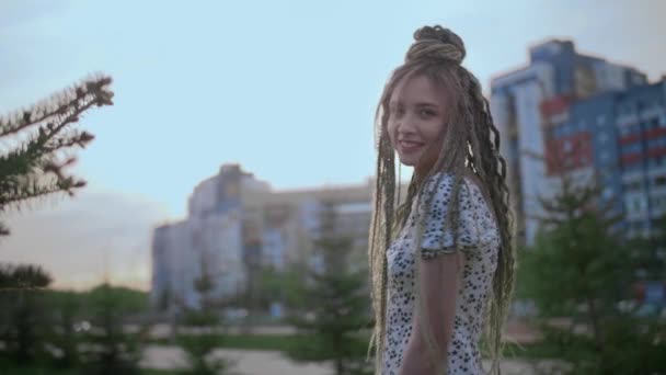 Uma menina jovem e feliz bonito com dreadlocks caminha pela rua e posa — Vídeo de Stock