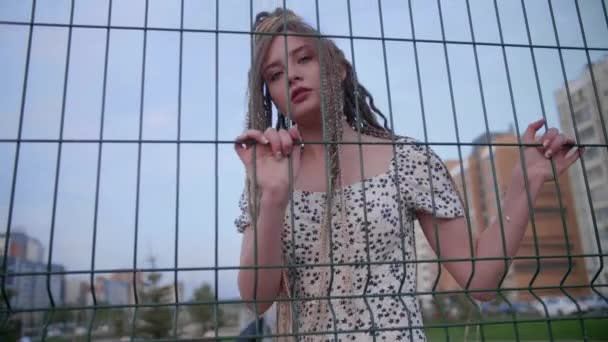 Молода дівчина з дредлоками позує на паркані — стокове відео