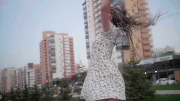 Uma menina jovem e feliz bonito com dreadlocks caminha pela rua e posa — Vídeo de Stock