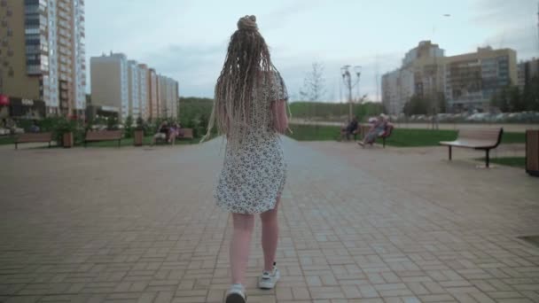 Een schattig jong en gelukkig meisje met dreadlocks loopt door de straat en poseert — Stockvideo