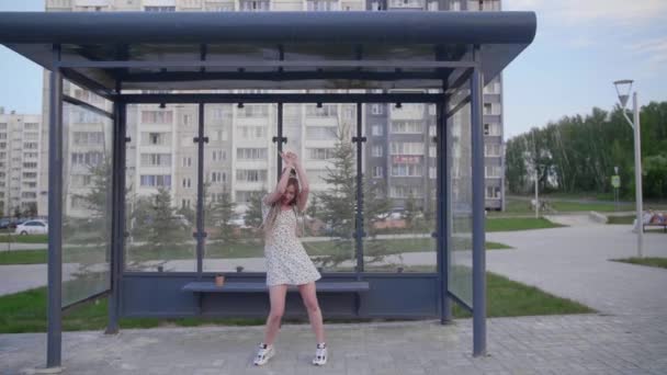 一个穿着浅色连衣裙的可爱女孩在巴士站跳舞 — 图库视频影像