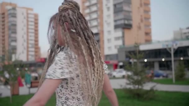 Uma menina jovem e feliz bonito com dreadlocks caminha pela rua e posa — Vídeo de Stock