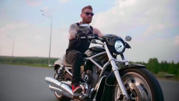 Un motard élégant avec des tatouages fait du vélo sur une route de campagne au coucher du soleil — Video