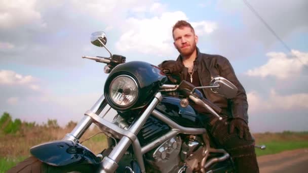 Młody człowiek siedzący na motocyklu na drodze o zachodzie słońca, zwolniony ruch — Wideo stockowe