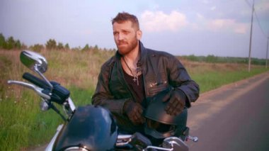 Gün batımında motosiklette oturan genç adam, ağır çekimde.