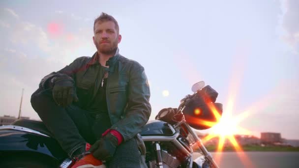 Jovem sentado na motocicleta na estrada ao pôr do sol, câmera lenta — Vídeo de Stock
