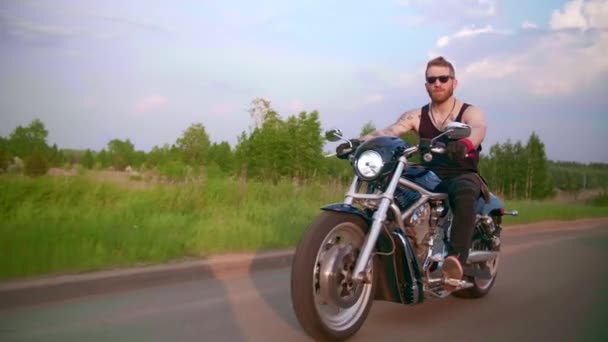 Motociclista elegante con tatuaggi guida una moto su una strada di campagna al tramonto — Video Stock