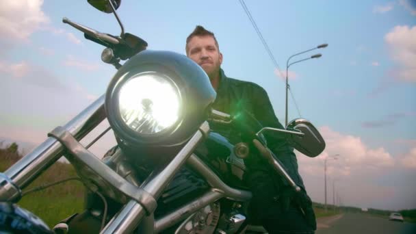 Młody człowiek siedzący na motocyklu na drodze o zachodzie słońca, zwolniony ruch — Wideo stockowe