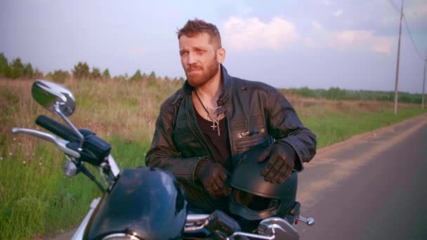 Młody człowiek siedzący na motocyklu na drodze o zachodzie słońca, zwolniony ruch — Wideo stockowe