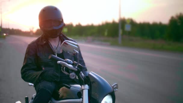 Jovem sentado na motocicleta na estrada ao pôr do sol, câmera lenta — Vídeo de Stock