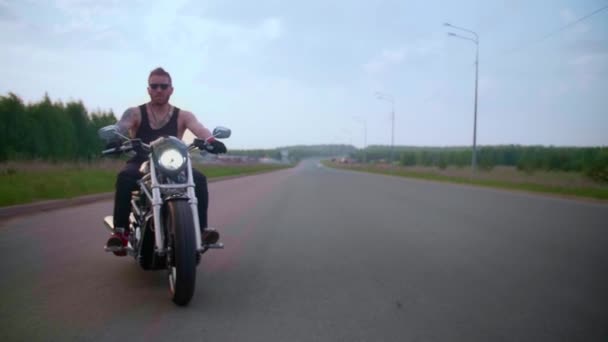Un motard élégant avec des tatouages fait du vélo sur une route de campagne au coucher du soleil — Video