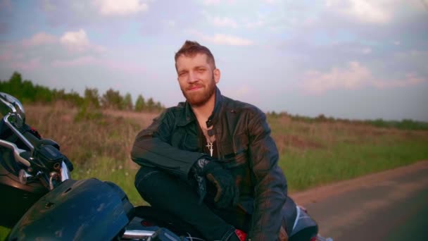 Joven sentado en motocicleta en la carretera al atardecer, cámara lenta — Vídeos de Stock