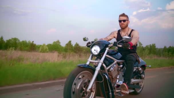 Stylischer Biker mit Tätowierungen fährt bei Sonnenuntergang Motorrad auf einer Landstraße — Stockvideo