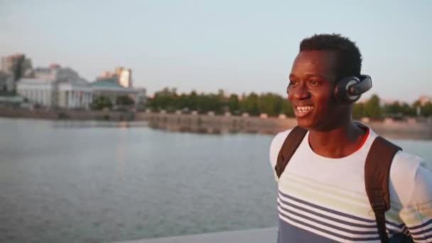 Gelukkige Afrikaanse man loopt en luistert naar muziek door draadloze headset in de stad — Stockvideo