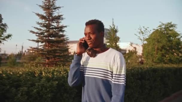 Porträtt glad glad glad ung svart kille i casual kläder, talar på smartphone promenad gata — Stockvideo