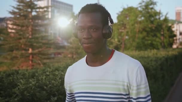 Black young man listens to music with headphones — Stock Video